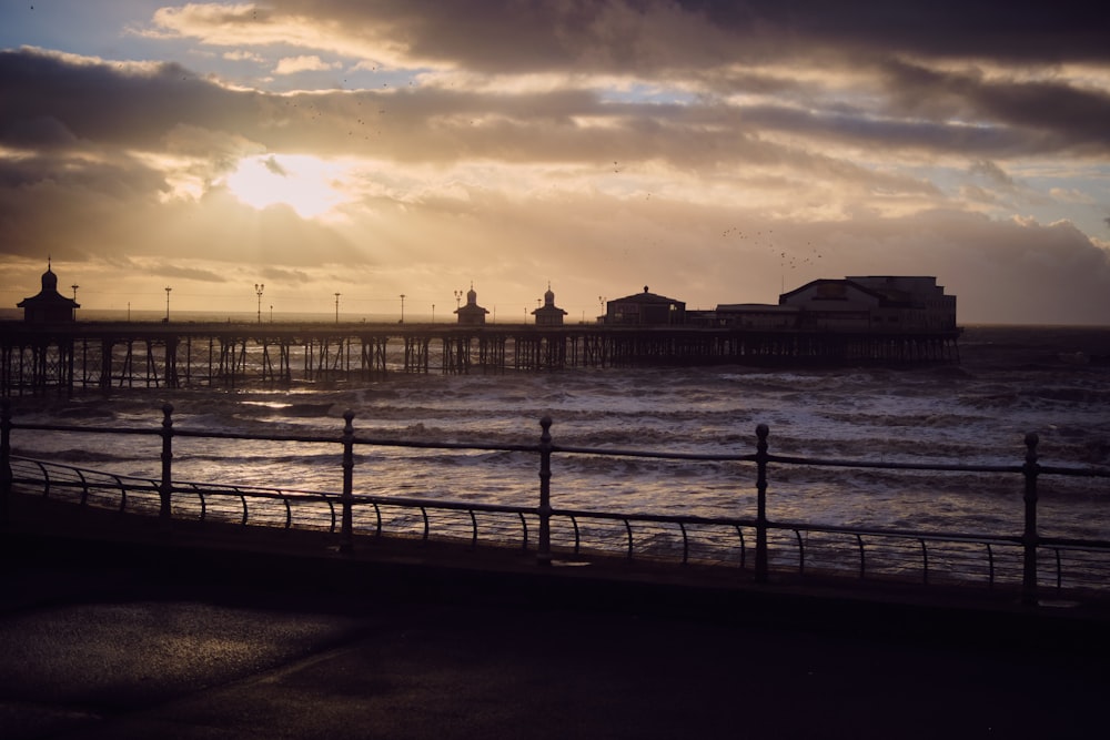 the sun is setting over the ocean with a pier in the background