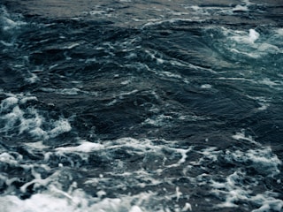 Dark ocean waves exhibit a dynamic and turbulent surface with white foam cresting over the deep, shadowy water.