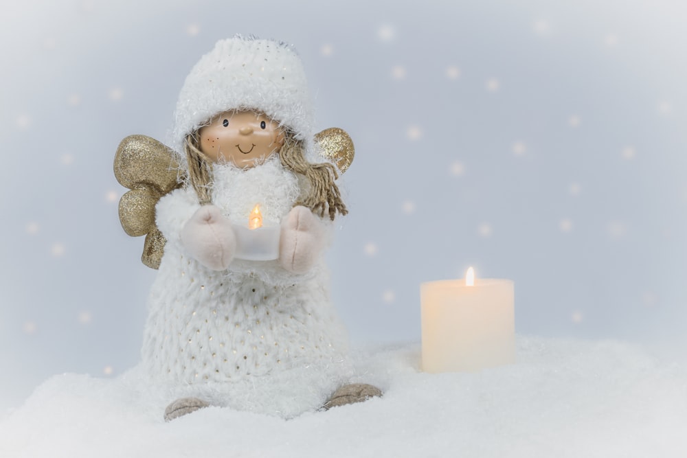 a small angel holding a lit candle in the snow