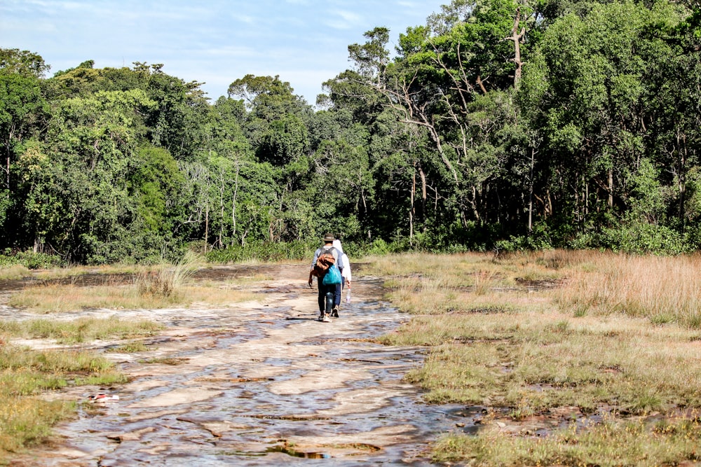 a woman walking down a dirt road in a forest