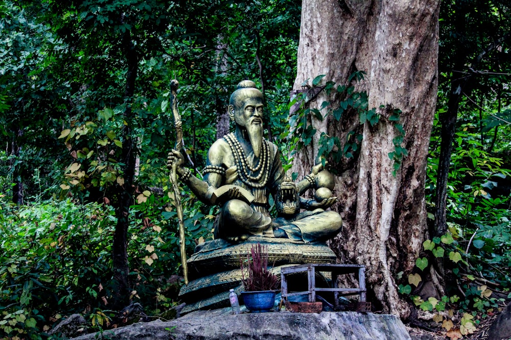 a statue of a man sitting on top of a bench next to a tree