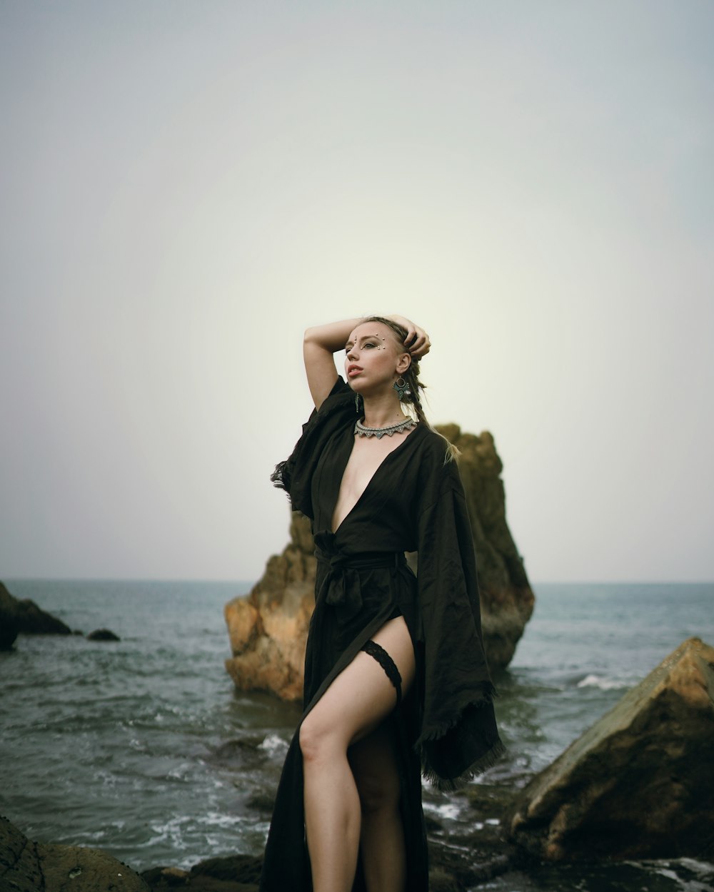 a woman in a black dress standing on rocks near the ocean
