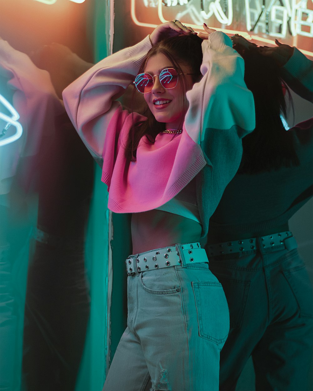 a woman in a pink shirt and jeans posing in front of a neon sign