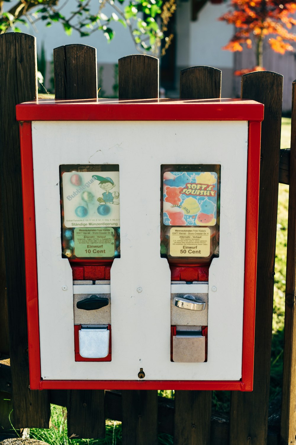 a red and white machine sitting next to a wooden fence