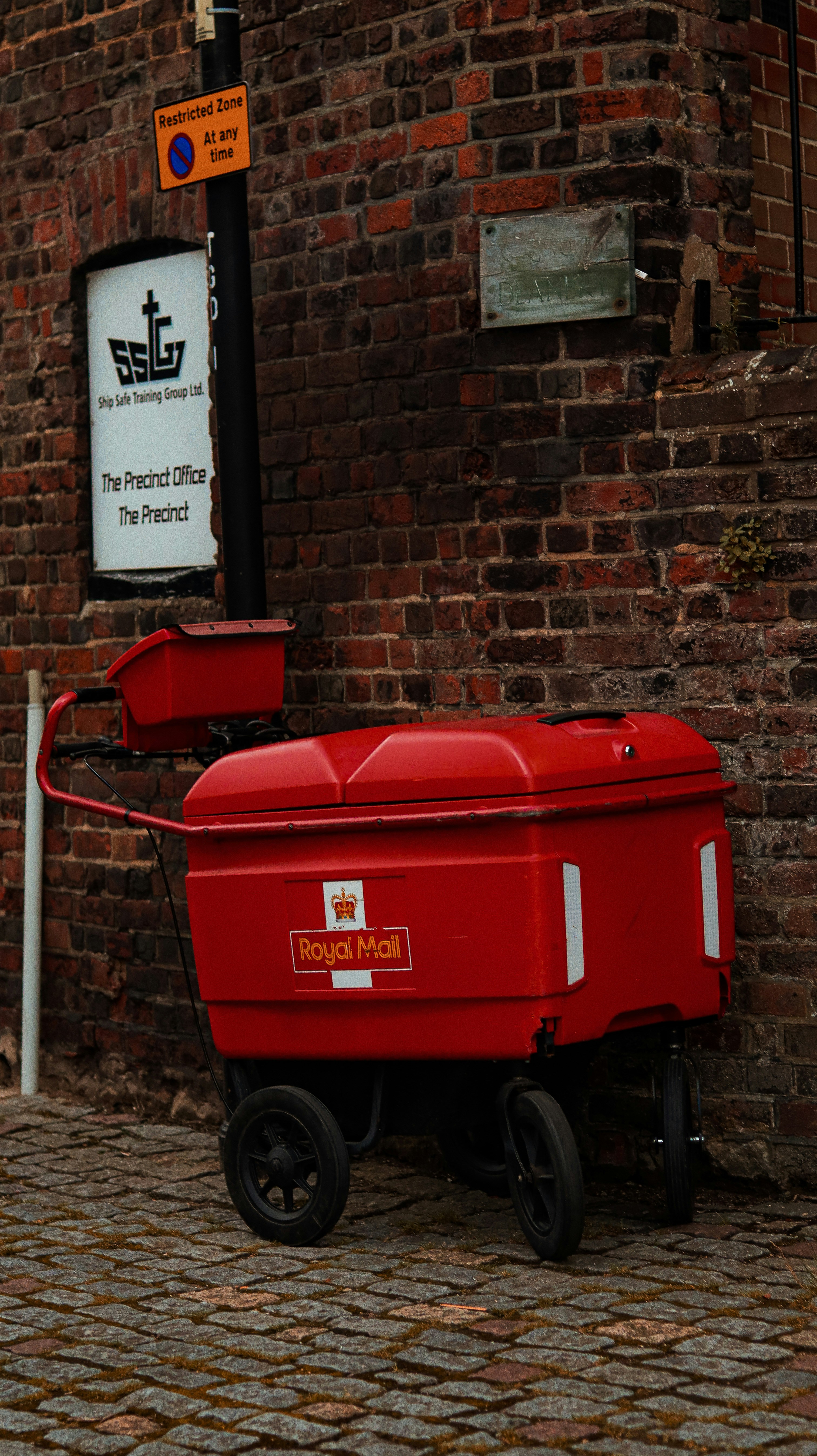 Carrito rojo de Royal Mail aparcado contra una pared de ladrillo