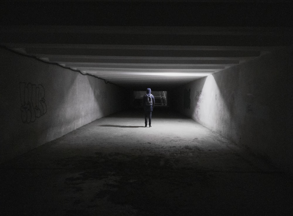 a person standing in a dark tunnel with graffiti on the walls