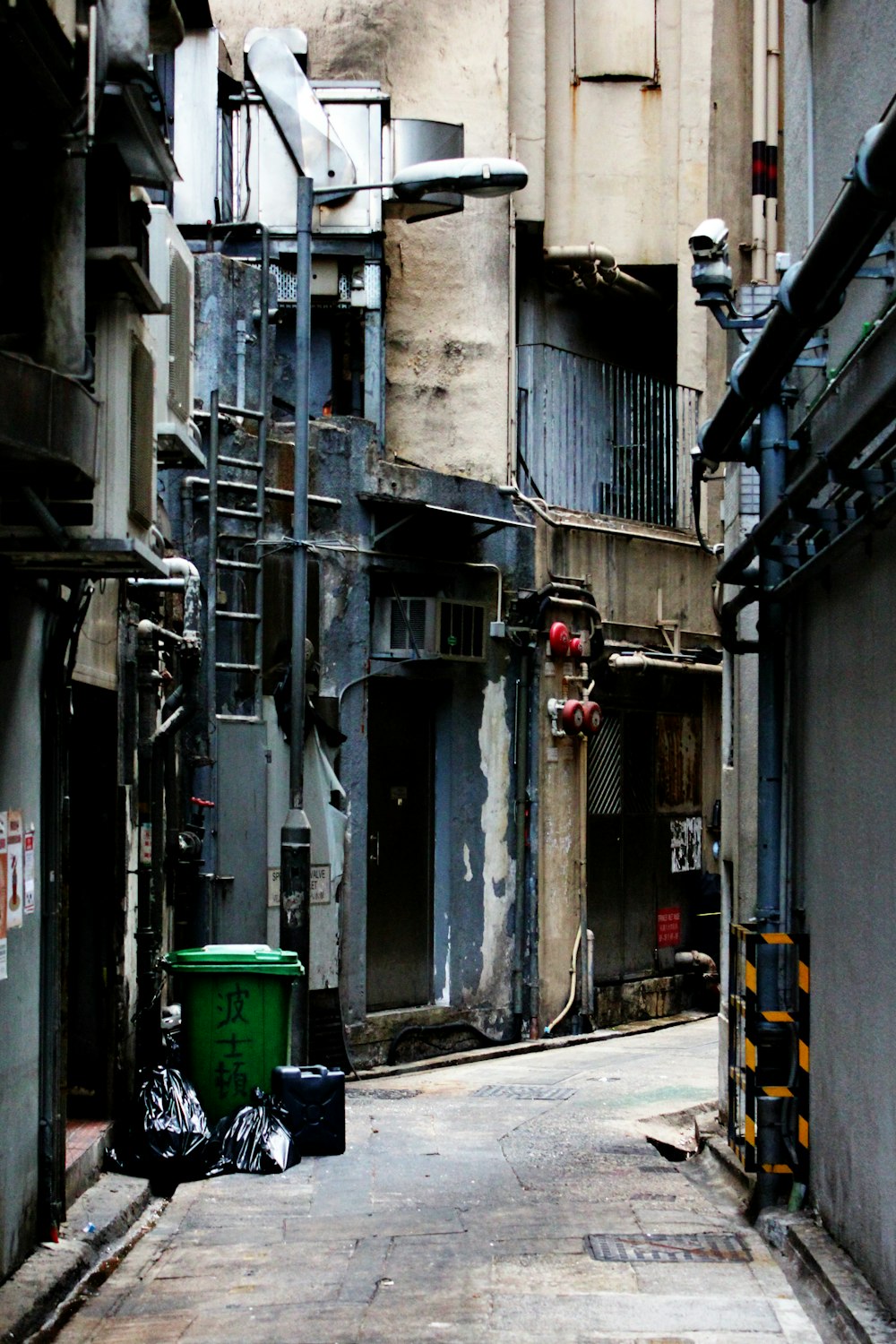 a narrow alley way with a green trash can