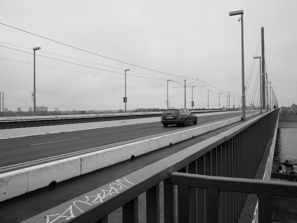 a black and white photo of a car driving over a bridge