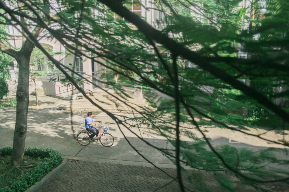 a man riding a bike down a street next to a tree