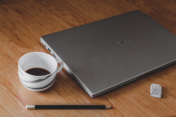 a laptop computer sitting on top of a wooden table next to a cup of coffee