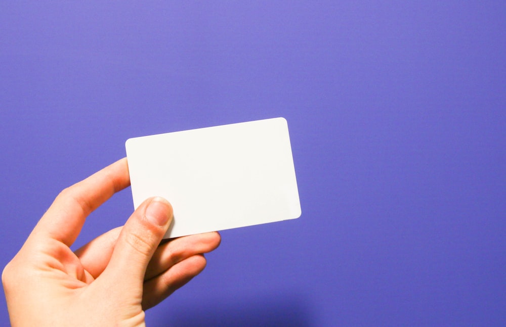 una mano che tiene un biglietto da visita bianco su uno sfondo viola