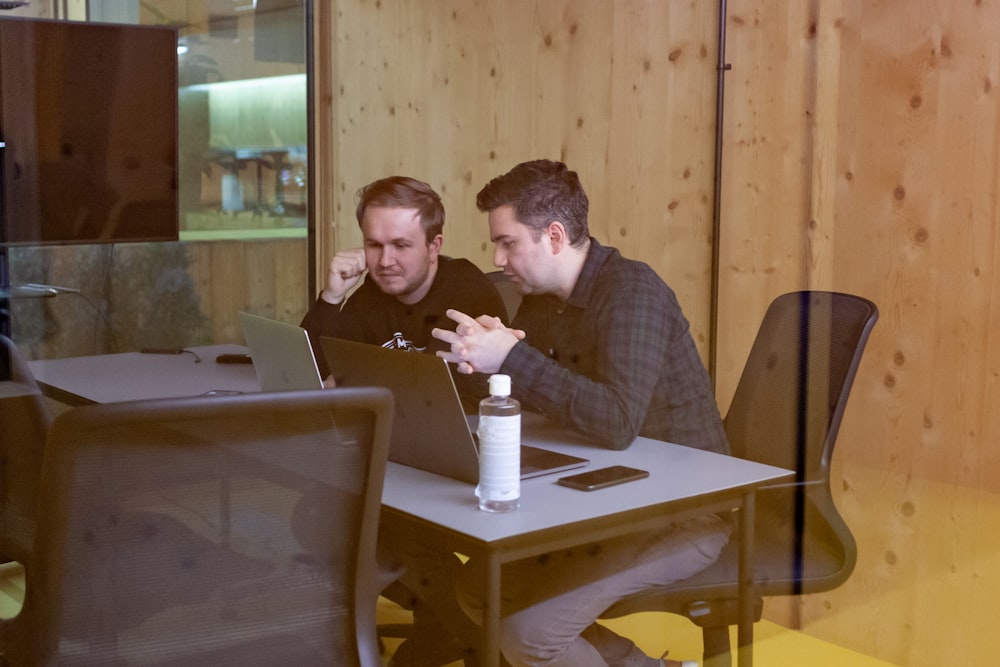 two men sitting at a table with a laptop