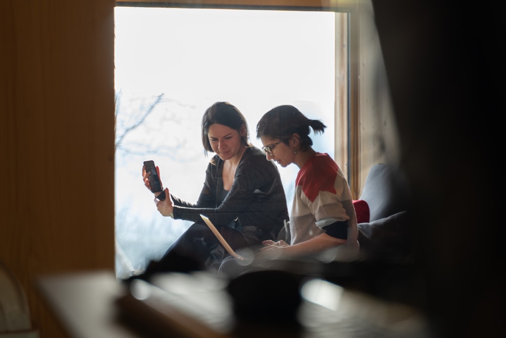 two women sitting on a couch looking at a cell phone