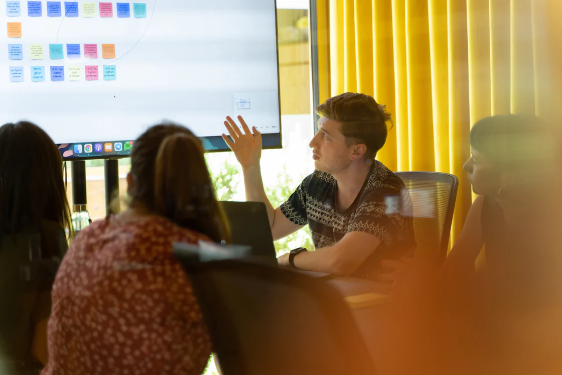 A man gives a presentation to colleagues beside a television screen