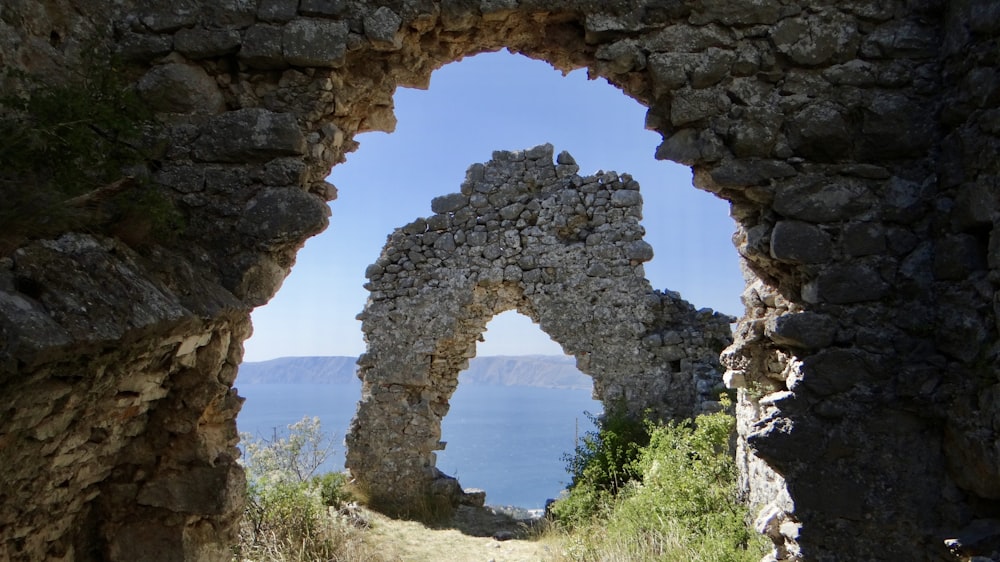 a stone arch with a view of a body of water