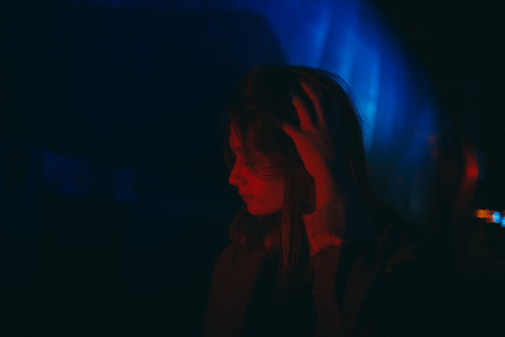 a woman standing in the dark with her hand on her head