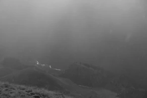 A moody black and white landscape with fog rolling over hills at dawn