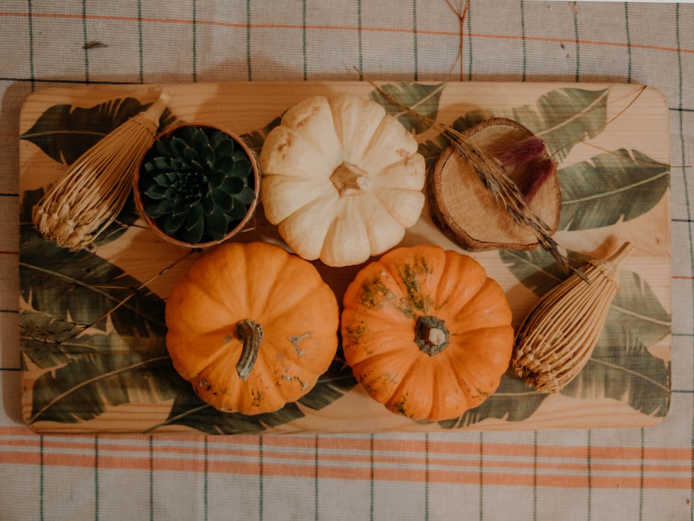 a wooden cutting board topped with pumpkins and leaves