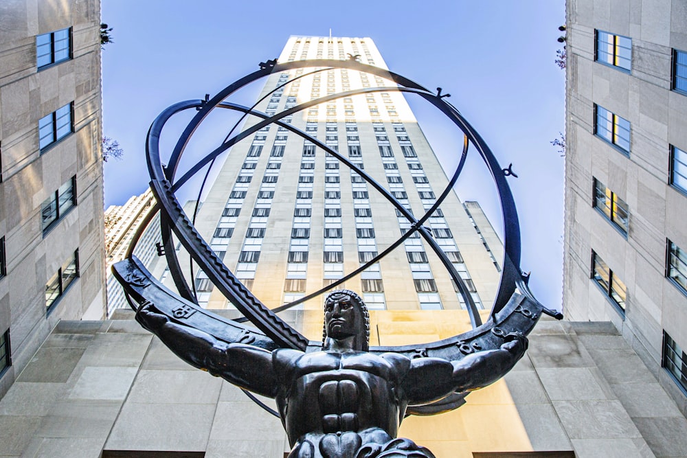a statue of a man holding a circle of life in front of a tall building