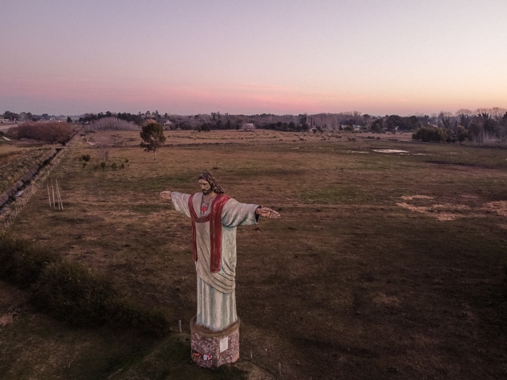 a statue of jesus in a field at sunset