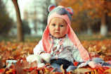 a baby wearing a knitted bear hat sitting in a pile of leaves