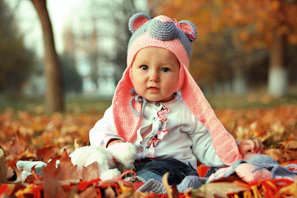a baby wearing a knitted bear hat sitting in a pile of leaves