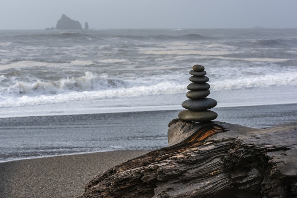 a stack of rocks sitting on top of a log near the ocean