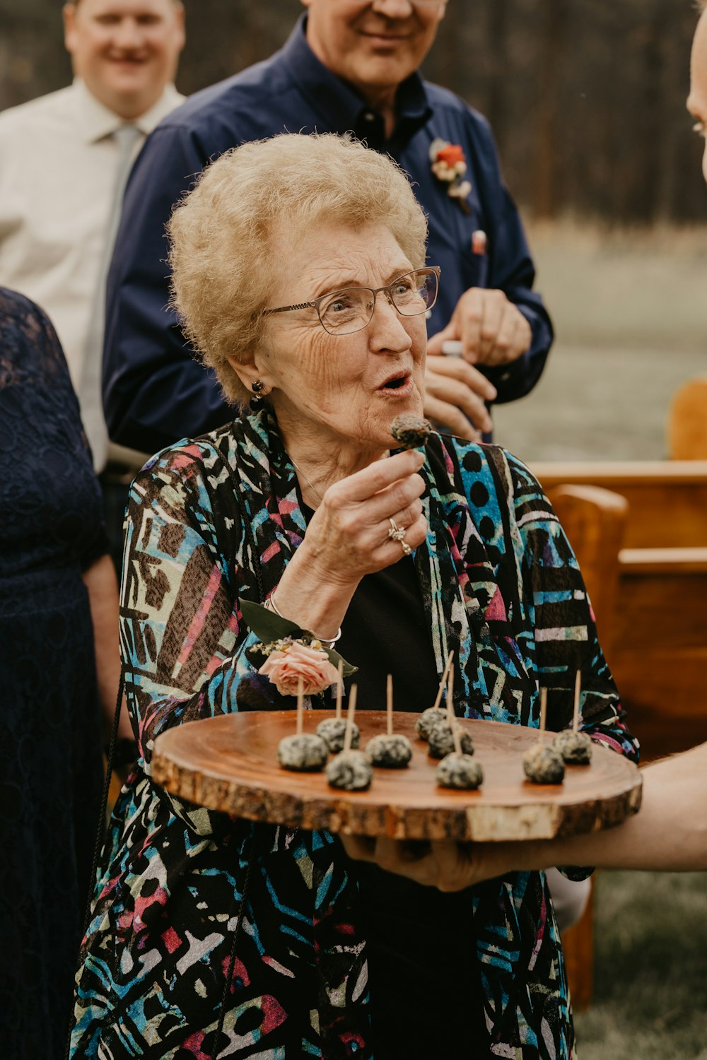 an older woman holding a tray of cupcakes