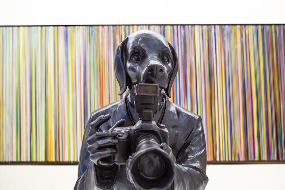 a statue of a man holding a camera in front of a painting