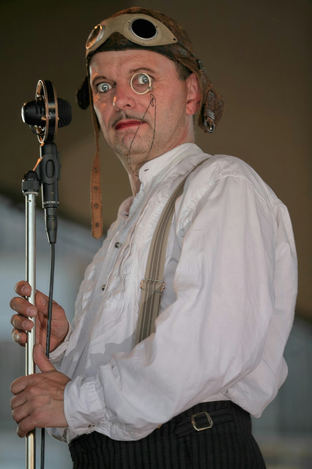 a man wearing a hat and suspenders holding a stick