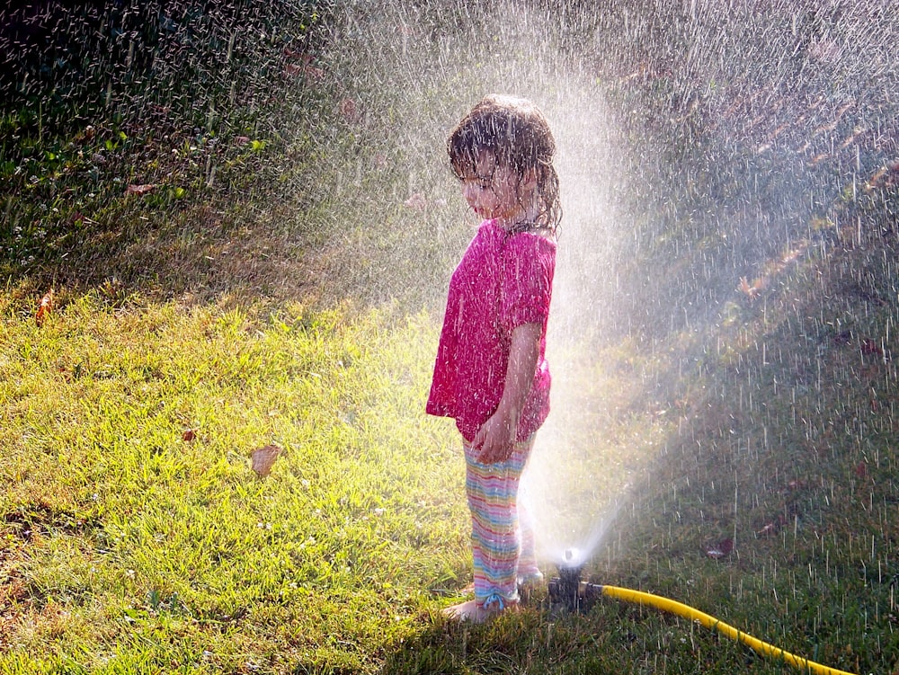 a little girl standing under a sprinkle of water
