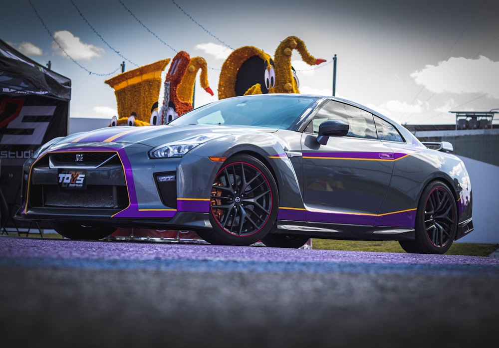 a grey sports car with purple stripes parked in a parking lot