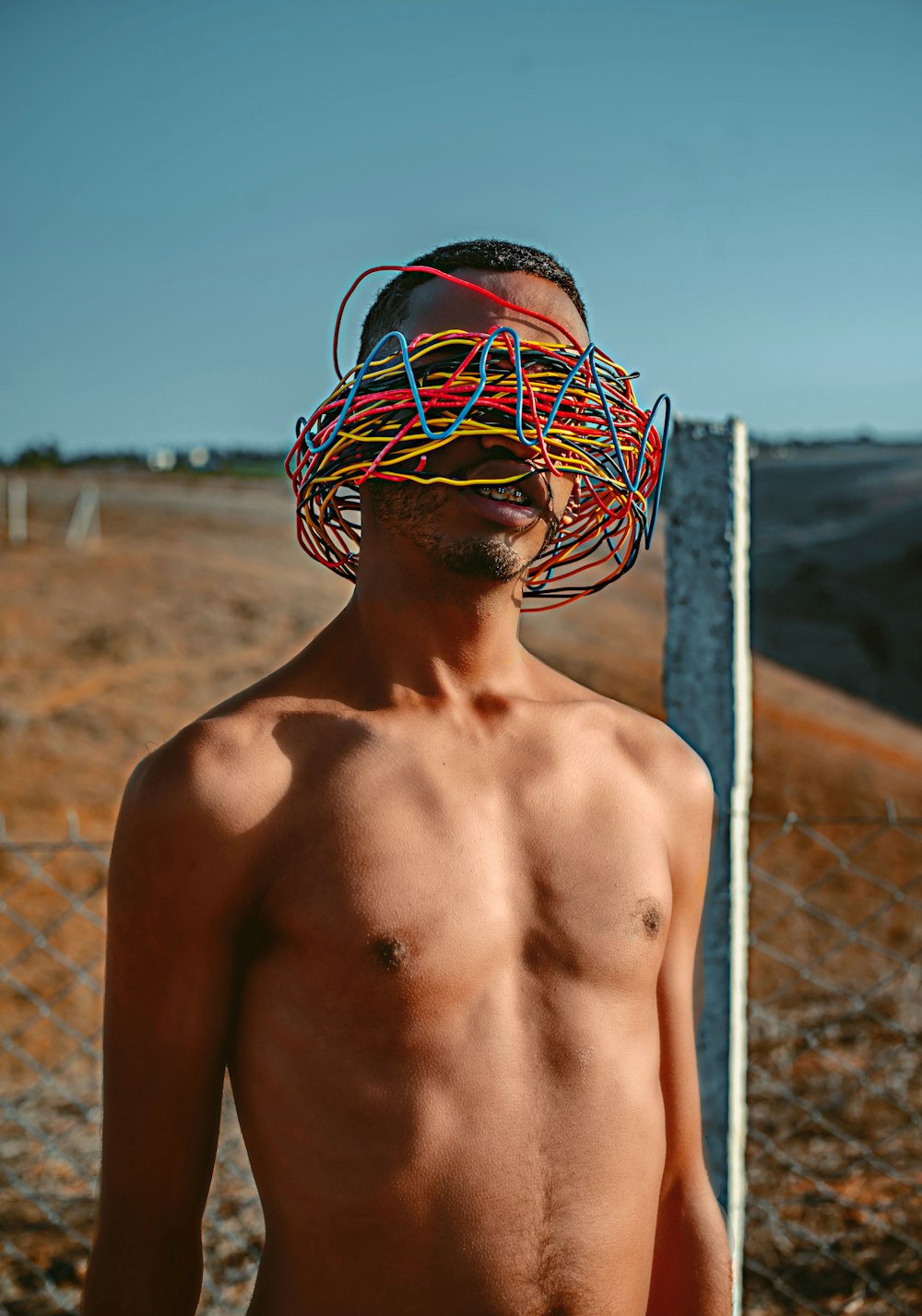 a shirtless man standing in front of a fence