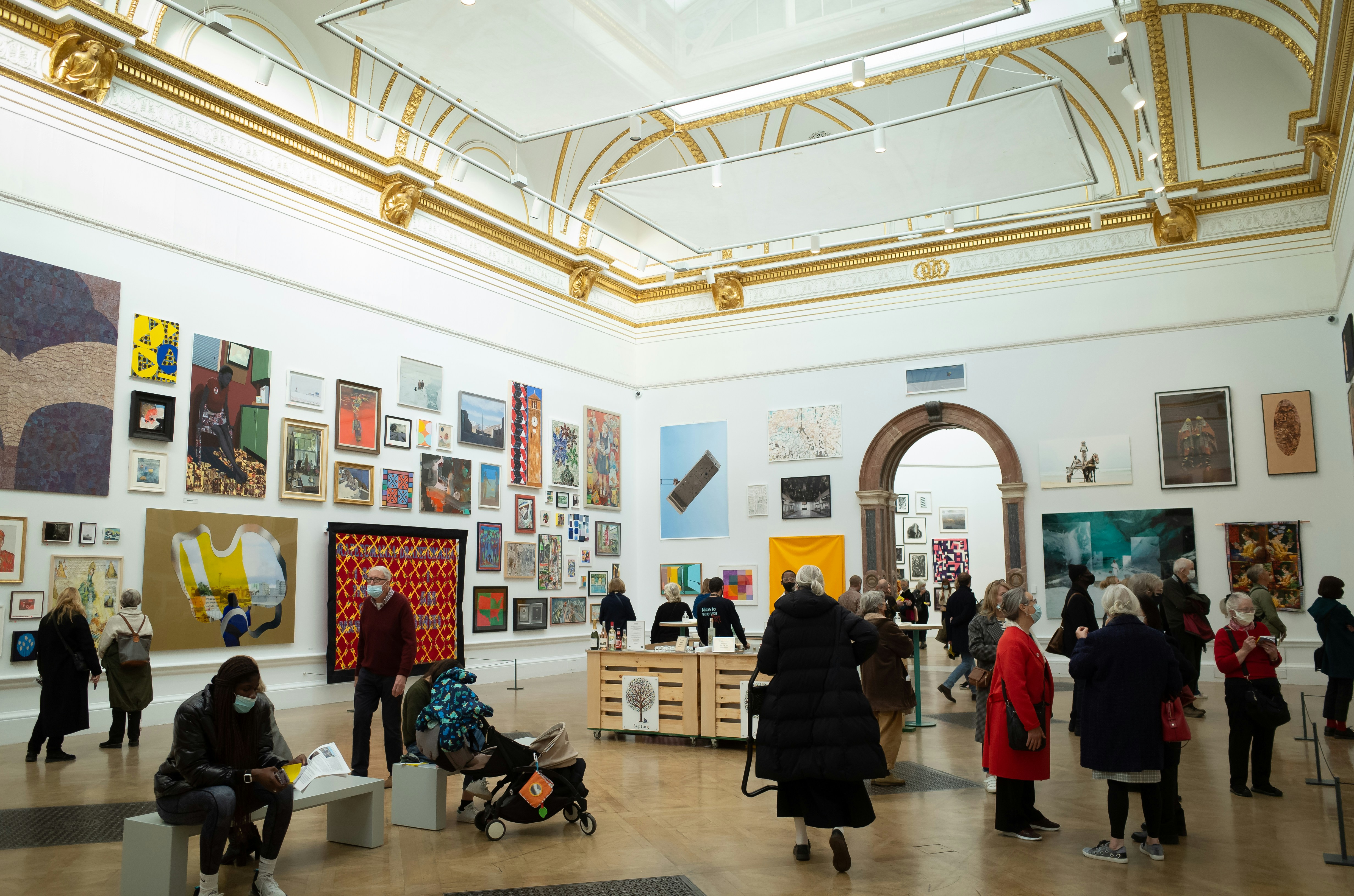 Gallery opening with white walls, hanging paintings and warm spotlights above a crowd of visitors