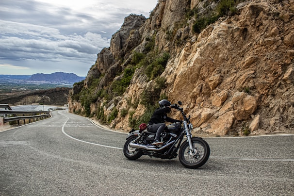 Rider wearing a rugged leather jacket and gloves, gripping handlebars on a winding mountain road