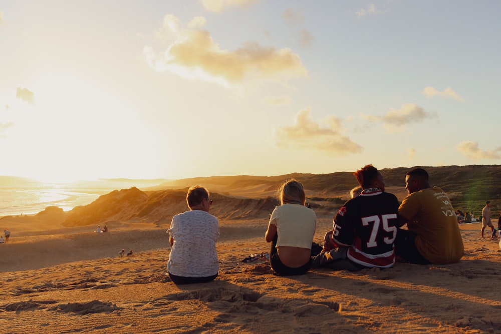 a group of people sitting on top of a sandy beach