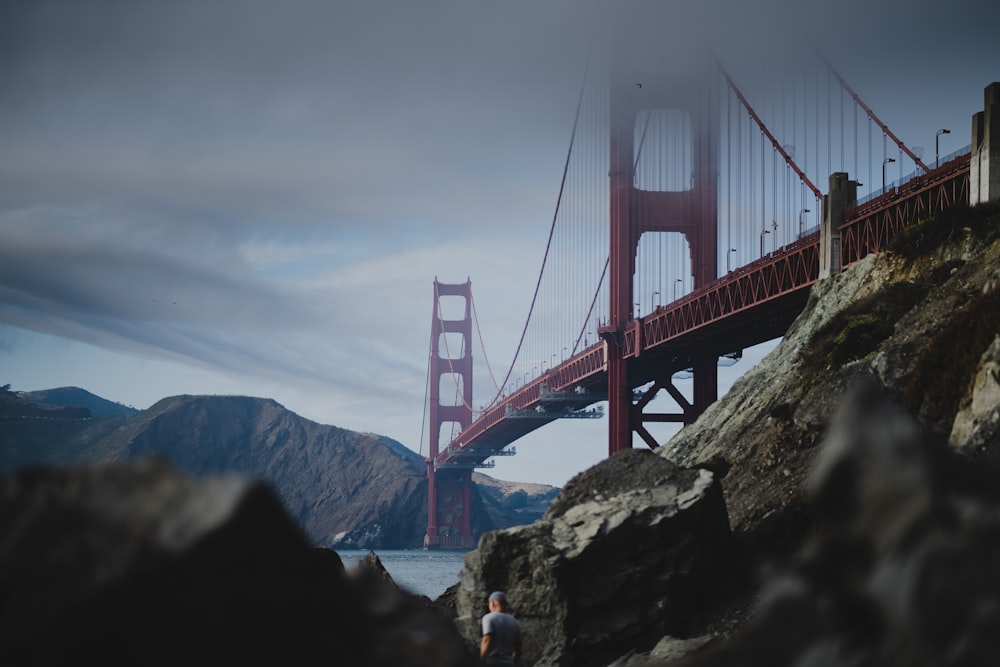 a person standing on a rock near a large bridge