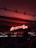 A dimly lit bar setting featuring a prominent neon sign reading 'Aperitivo Bar' in bright red. Shelves stocked with various bottles of liquor are visible beneath the sign. The lighting creates a warm and inviting atmosphere, with a person silhouetted in the foreground.
