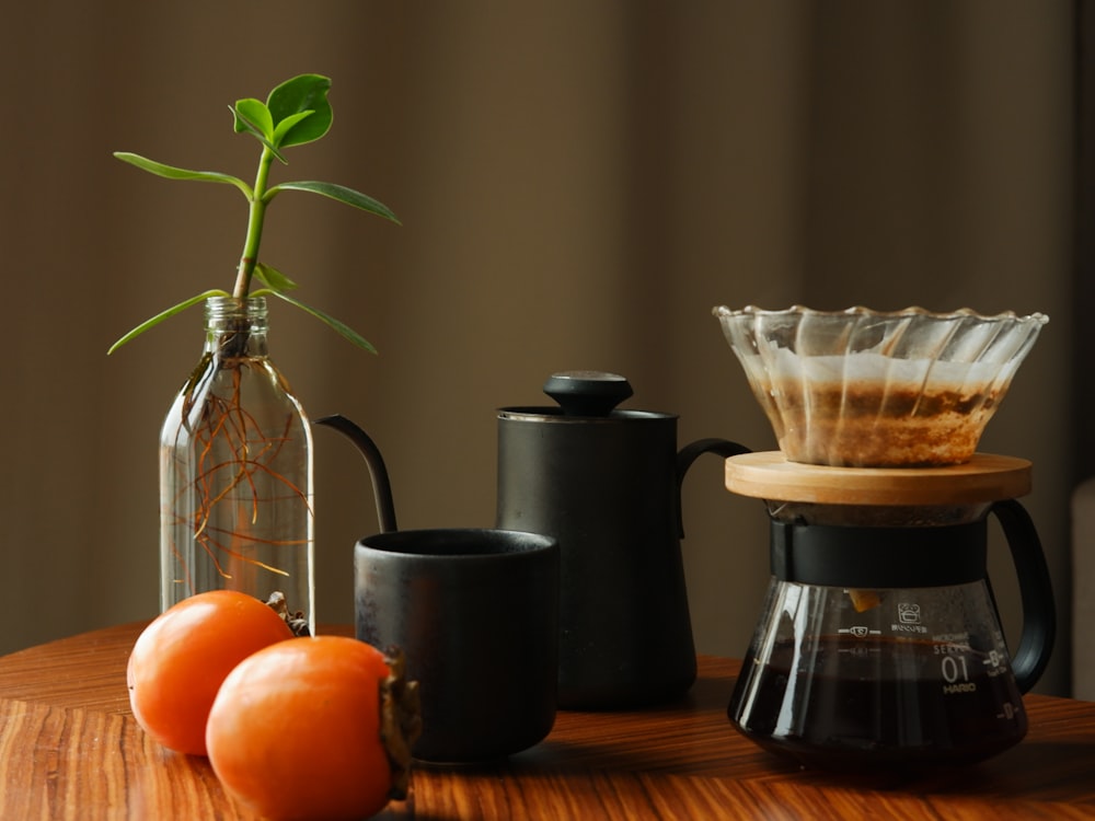 a wooden table topped with two oranges and a coffee pot