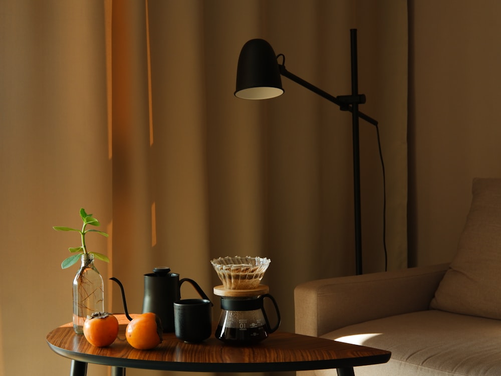 a table with a coffee pot, a lamp, and some fruit on it