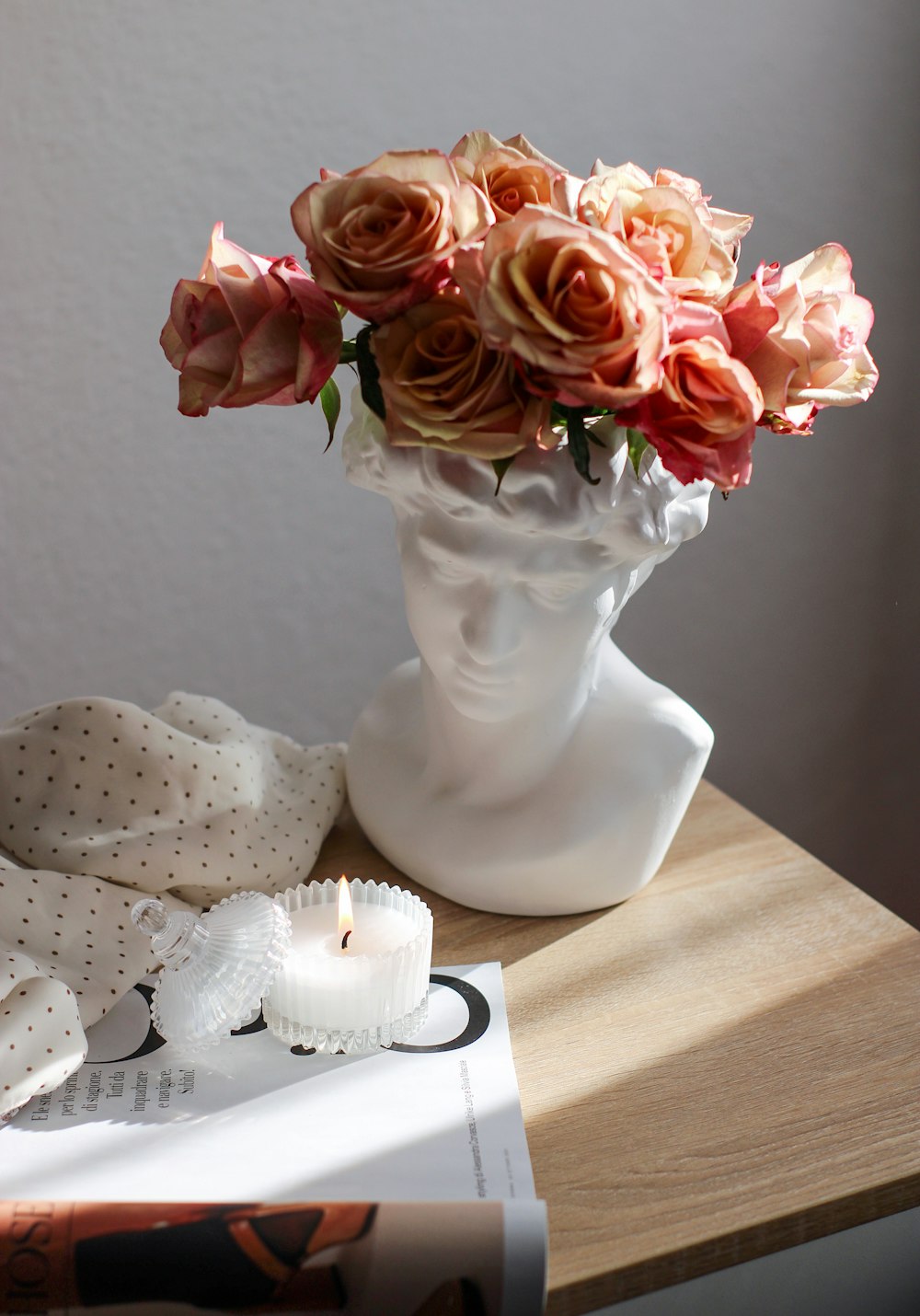 a vase of roses on a table with a candle