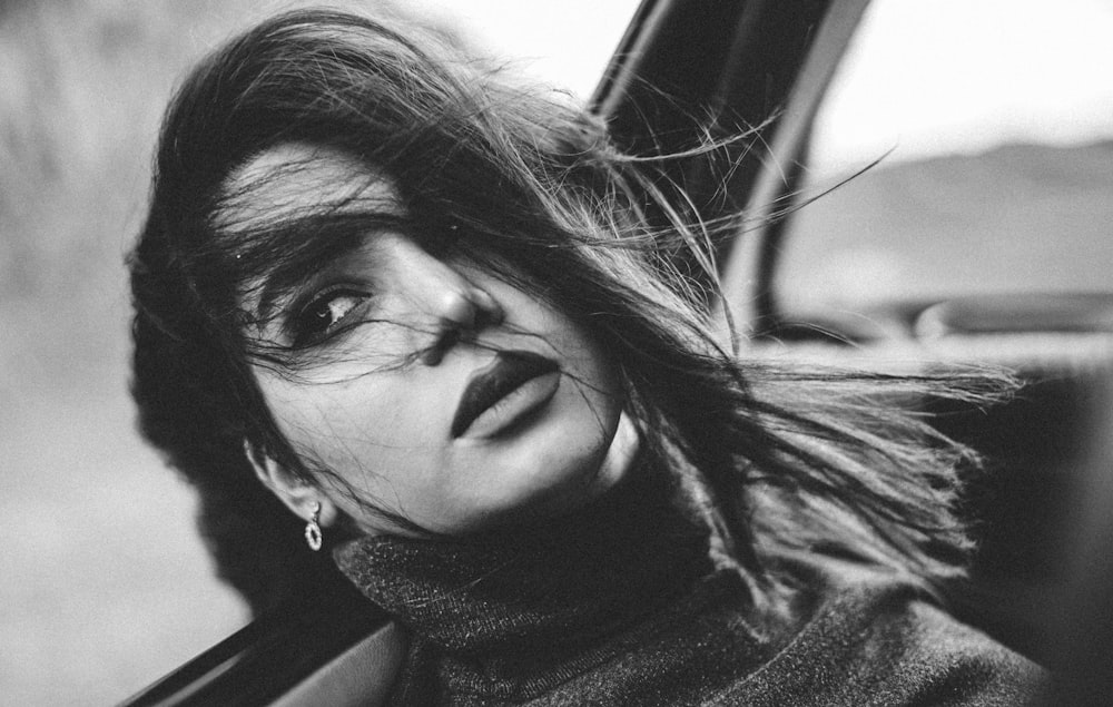 a black and white photo of a woman sticking her head out of a car window