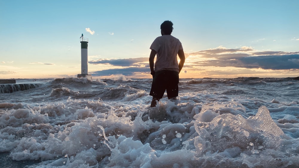 a man standing in the ocean with a lighthouse in the background