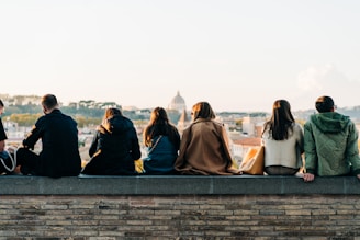 a group of people sitting on top of a brick wall