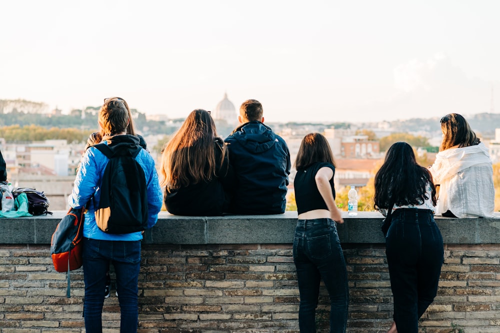 a group of people sitting on top of a brick wall