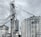 A large industrial scene featuring multiple metal silos and storage tanks set against a cloudy sky. The structures are interconnected by various walkways and pipes. The image highlights a complex network of steel frameworks and cylindrical storage units.