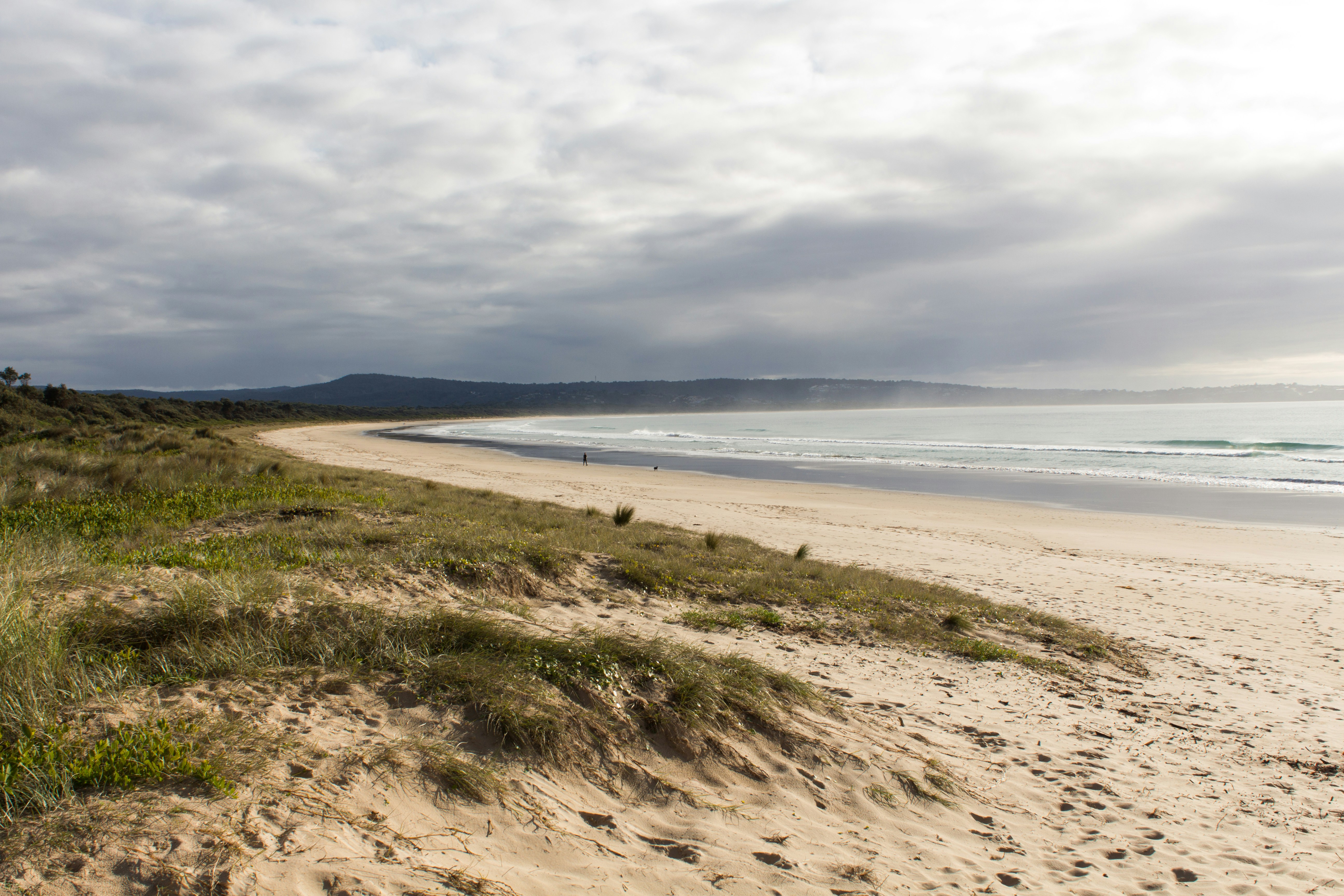 a sandy beach next to the ocean under a cloudy sky