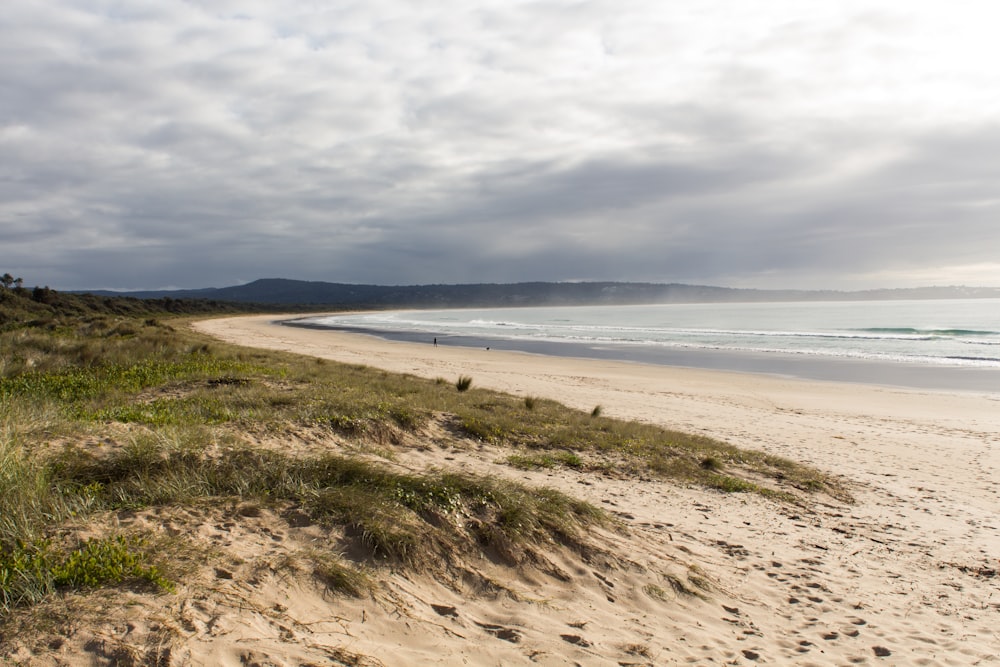 a sandy beach next to the ocean under a cloudy sky