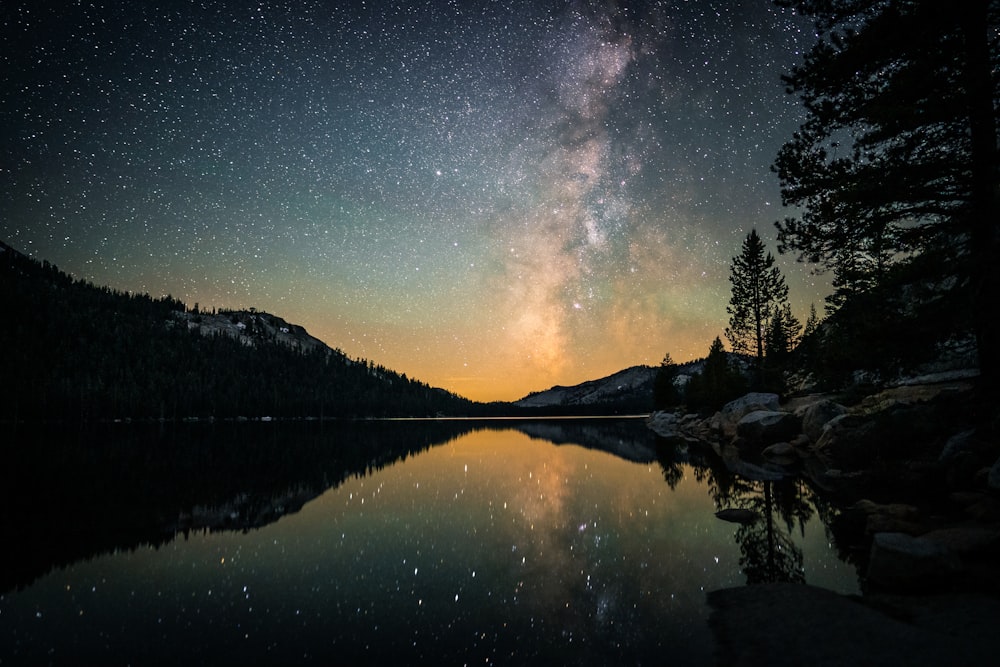 a lake surrounded by trees under a night sky