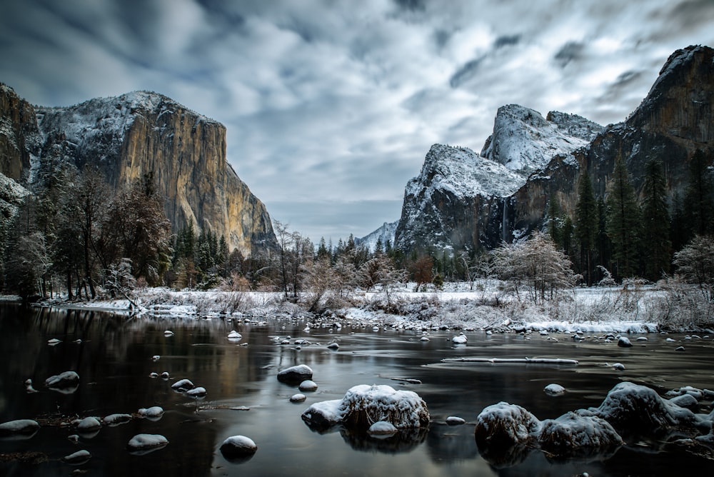 a river surrounded by snow covered mountains under a cloudy sky